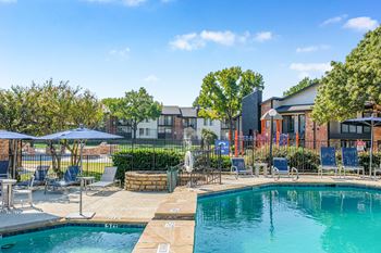 A swimming pool surrounded by lounge chairs and umbrellas with a building in the background.